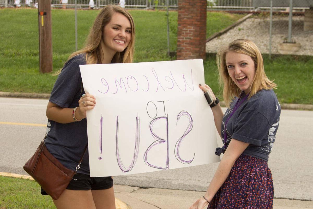 两个女孩举着海报，上面写着欢迎来到S-B-U